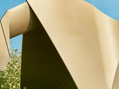 An large origami-style sculpture is displayed beside a field of wildflowers under a blue sky.