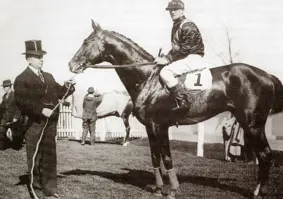 Black and white photo of Edward standing next to horse and jockey holding bridle
