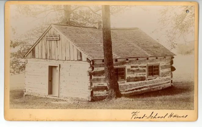 Black-and-white exterior view of the 1894 one-room schoolhouse near Waterloo Park, with students and teacher posed outside its wooden structure.