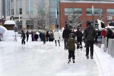 People ice skating on outdoor rink in Waterloo Public Square with urban buildings in the background. 
