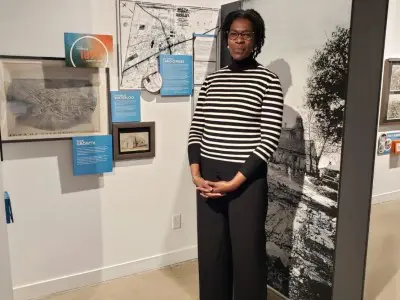Photo of Peggy Plet in front of exhibit banner with photo of Levi Carroll