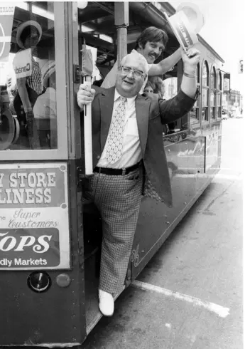 Charlie on a trolley waving to the people on the streets
