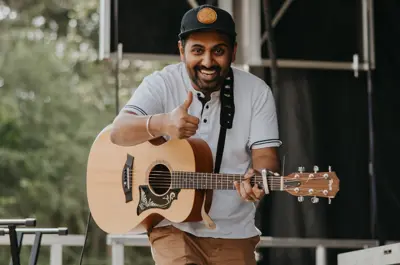 Singer smiles at camera with a thumbs up while performing on stage during an outdoor event.