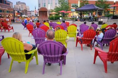 A group of people sitting in colourful muskoka chairs observing a live musical performance in Waterloo Public Square.