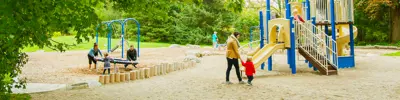 Families with young children playing on swings and climbing equipment in a park.