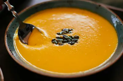 Close-up of pumpkin soup garnished with seeds in a ceramic bowl.