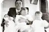 Black and white photo of Edward sitting with two babies on his lap and a small child standing beside.