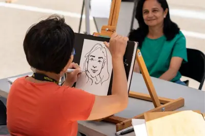 An artist sketches a person's portrait on a canvas at an outdoor event. 