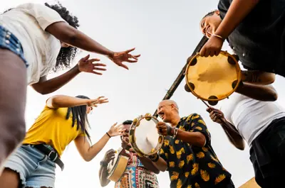 A group of people joyfully playing tambourines and dancing outside, viewed from below against a clear sky.