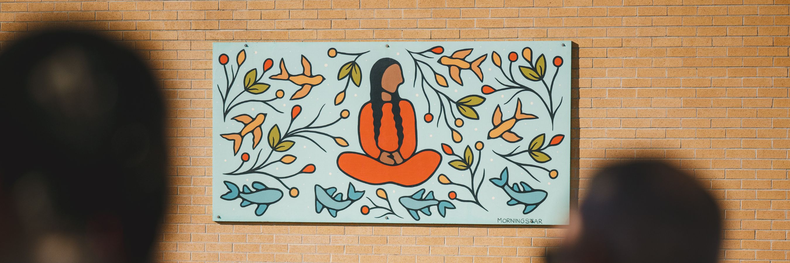 A mural on a brick wall showing a person sitting cross-legged, surrounded by bright leaves, flowers and birds.
