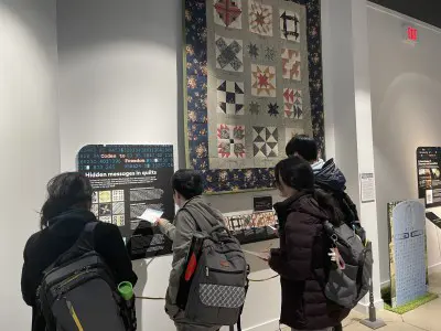 Group of people reading text panel and looking at quilt hung on wall