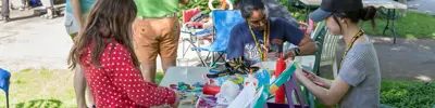 Children and volunteers making crafts together at an outdoor table.
