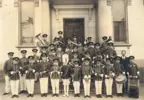 Black and white photo of the young Elmer Kutt and other boys in band uniform holding instruments and standing on the front steps of an unidentified building.