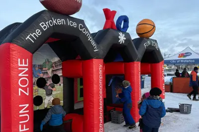 A group of kids play with giant inflatable sports game at outdoor winter event.