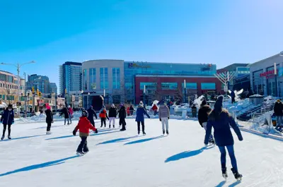 A group of people skating in the Waterloo Public Square on a sunny day.