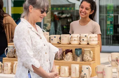 two people engaging under outdoor stall with a display of ceramic products including mugs and coasters.