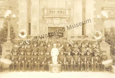 Historic Waterloo M.S. Band posing with instruments on the steps of a large columned building, with the band leader standing at the centre.