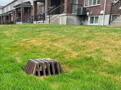 Diagram of a rear-yard catch basin: shows a grate at ground level that leads into an underground box and pipe to collect surface runoff water toward the storm sewer.