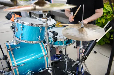 Person playing a set of vibrant blue drums outdoors on a paved sidewalk.