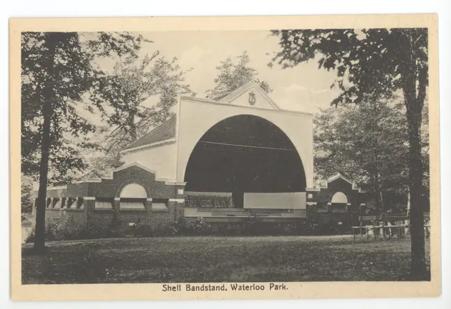 Open-air shell bandstand (semi-circular structure) in Waterloo Park, set on a manicured lawn and surrounded by trees.