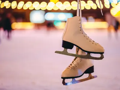 A pair of white figure skates hang above an outdoor rink lit with warm lights.