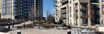 An outdoor plaza between residential towers with paved walkways, seating areas, young trees and lighting posts, creating a shared public space.