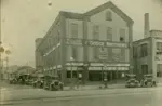 Black and white photo of garage with early dodge cars parked in front